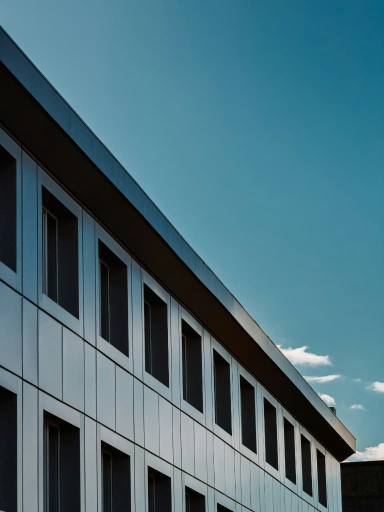 Looking up along a modern building facade against a clear blue sky